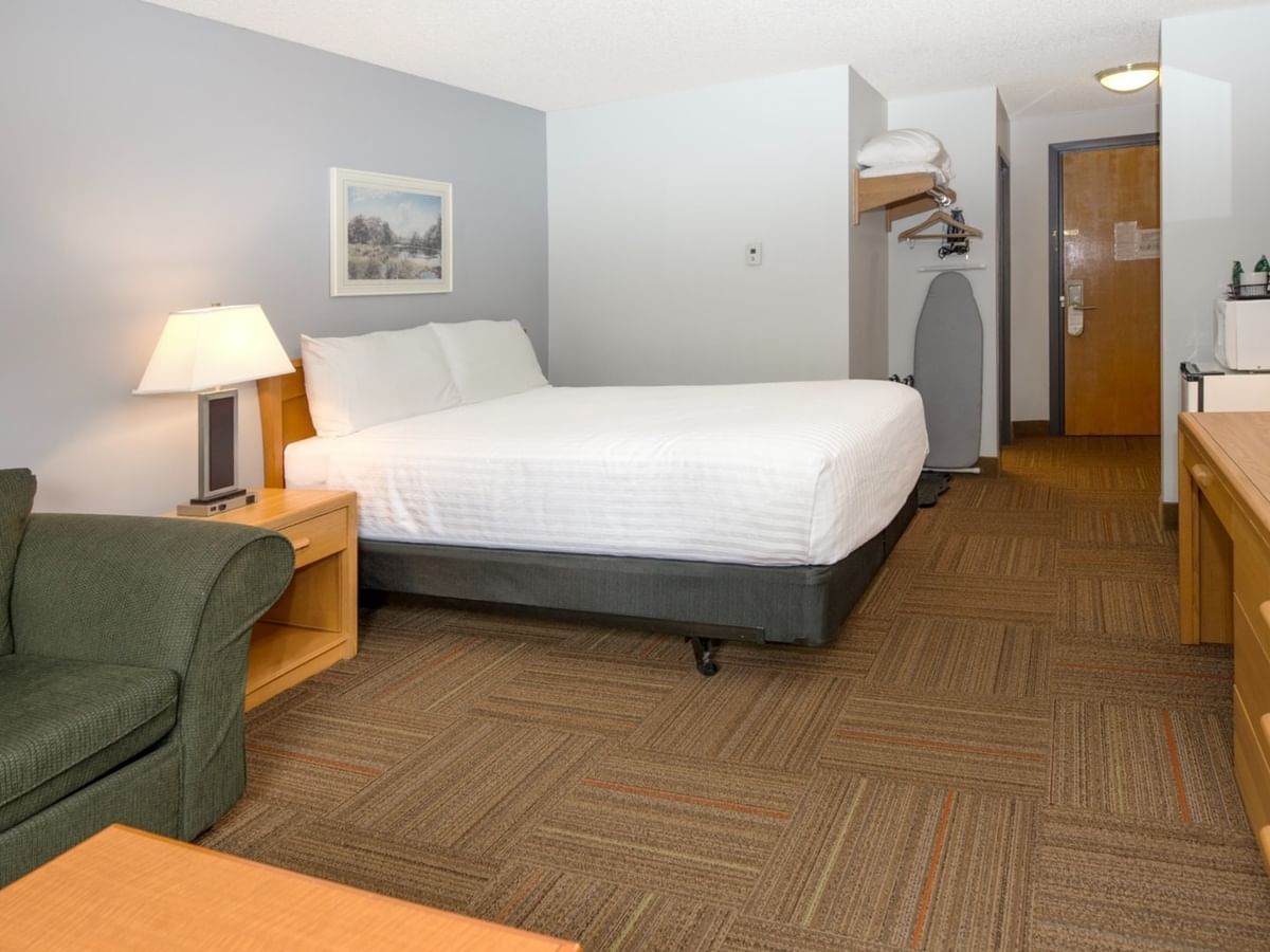 A hotel room with a bed, couch, nightstand, TV, and wooden dresser.