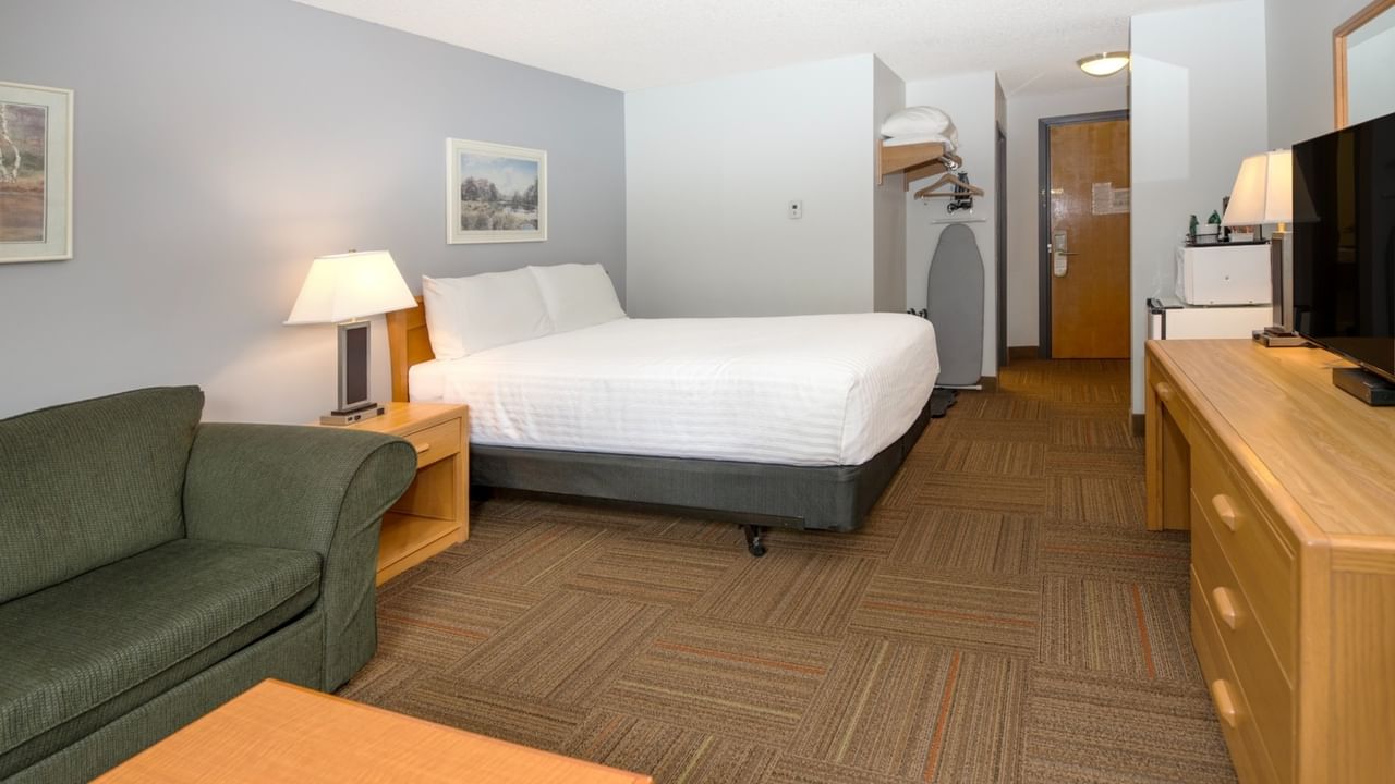 A hotel room with a bed, couch, nightstand, TV, and wooden dresser.