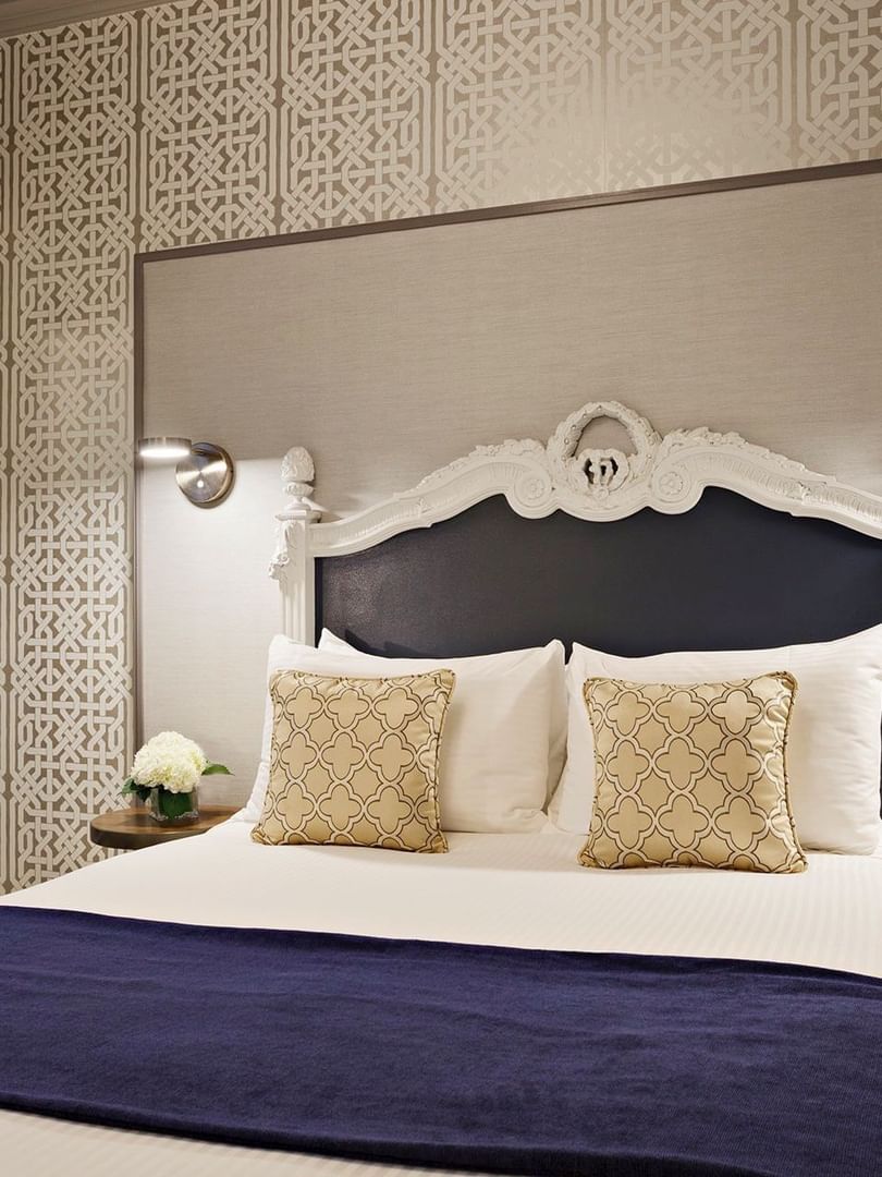 Ornate white bed by a mirrored wardrobe under geometric wallpaper in Deluxe Queen Room at Warwick San Francisco
