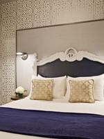 Ornate white bed by a mirrored wardrobe under geometric wallpaper in Deluxe Queen Room at Warwick San Francisco