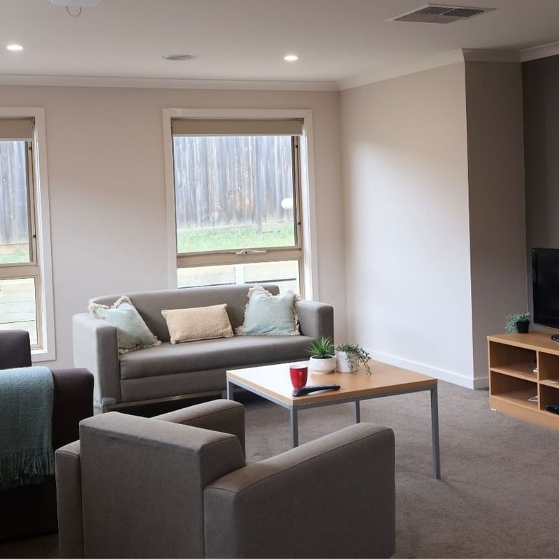 Comfortable living room with couches, coffee table, TV, and windows at La Trobe University Regional Housing – Melton.