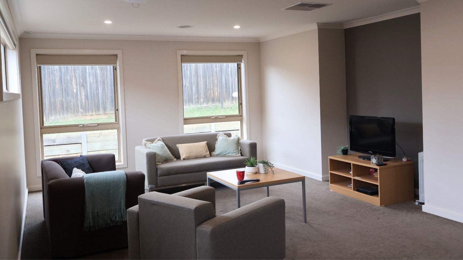 Comfortable living room with couches, coffee table, TV, and windows at La Trobe University Regional Housing – Melton.