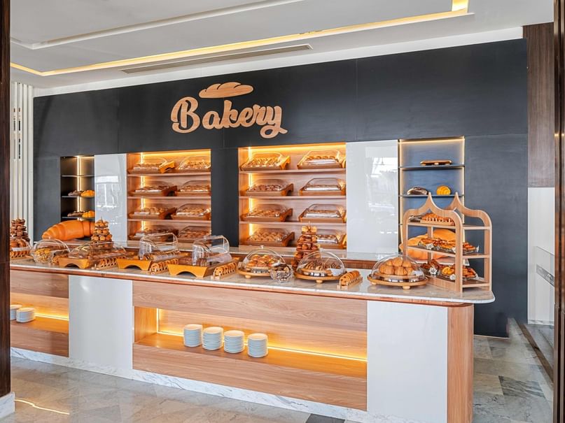 Bakery display with various pastries and bread, wooden counter, and illuminated shelves against a black wall.