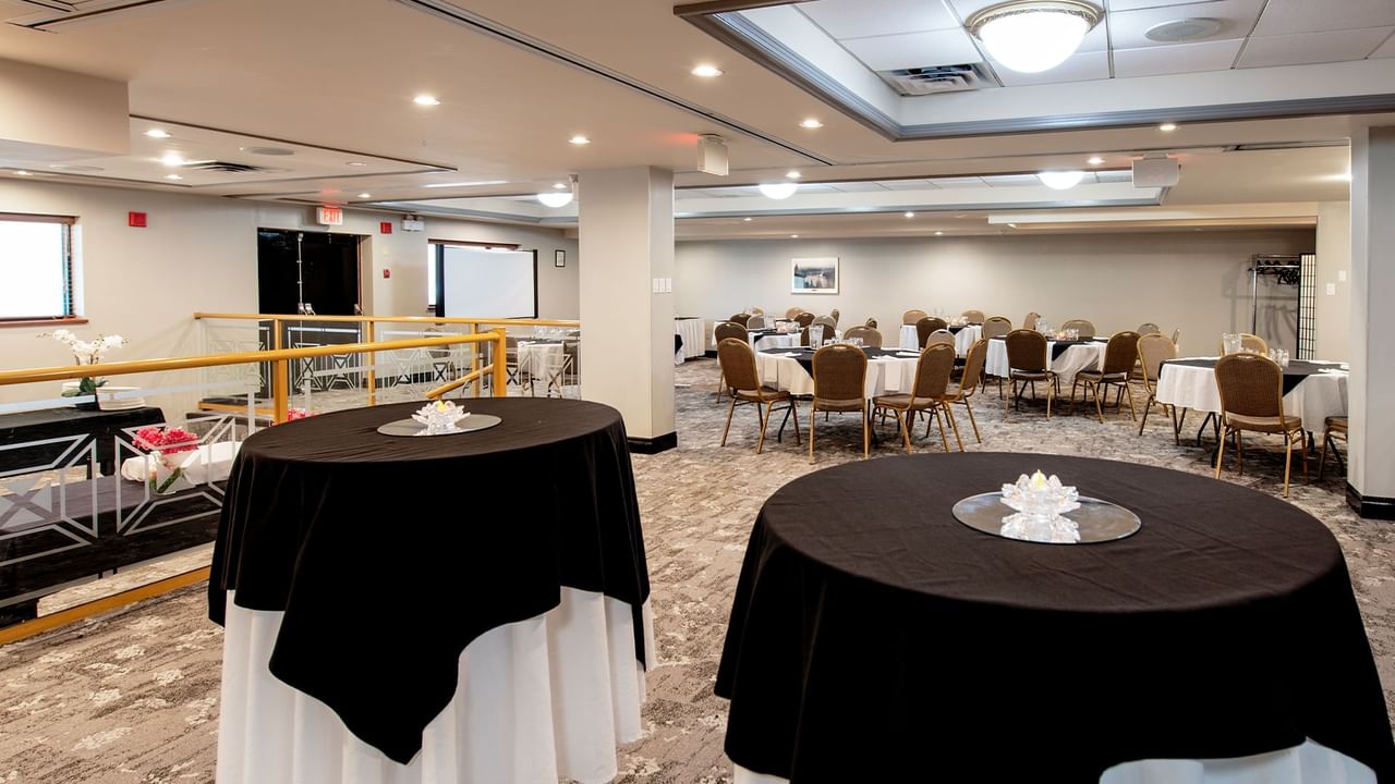Two round tables with black tablecloths and white napkins in a large event hall.