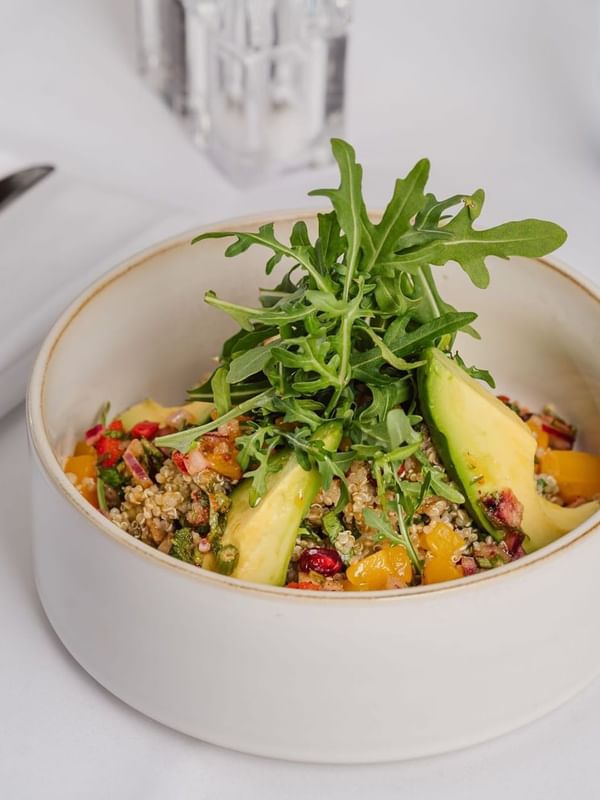 Fresh quinoa salad with avocado in a white bowl by a fork on a cloth table at Warwick Geneva