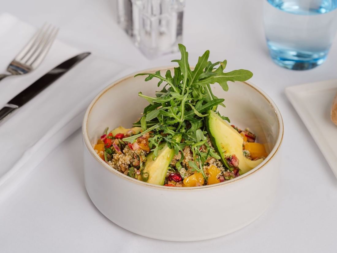 Fresh quinoa salad with avocado in a white bowl by a fork on a cloth table at Warwick Geneva