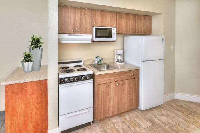 A compact kitchenette with a stainless steel sink, white refrigerator, white stove, microwave, and coffee maker.