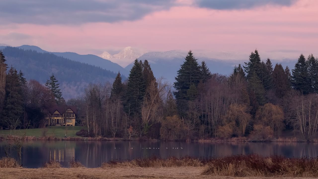 Deer Lake Park features a tranquil lake reflecting trees and mountains under a pink and purple twilight sky.