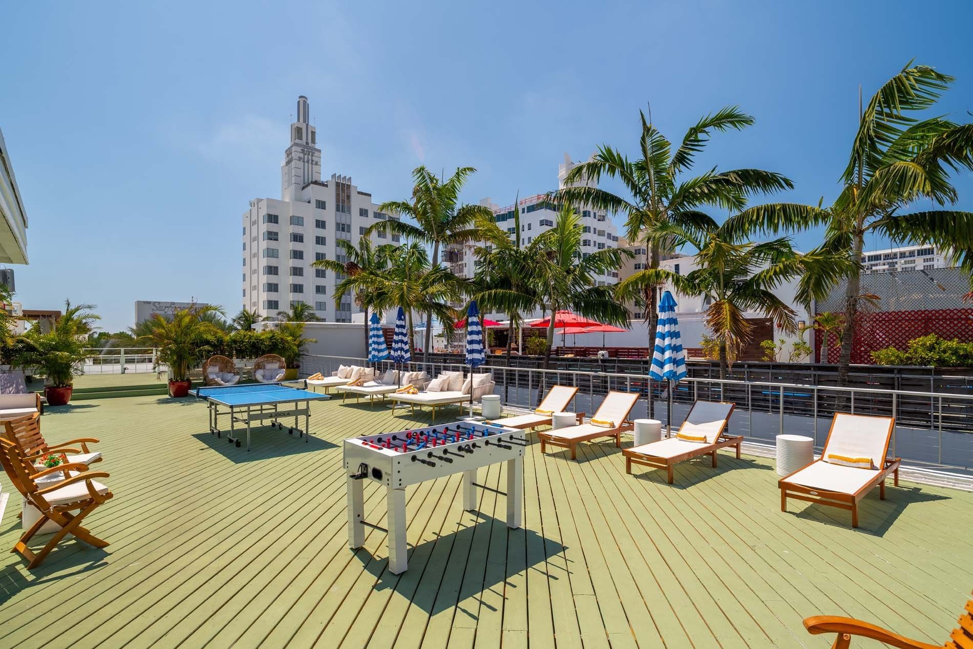 A rooftop deck with lounge chairs, foosball and ping pong tables, and palm trees.