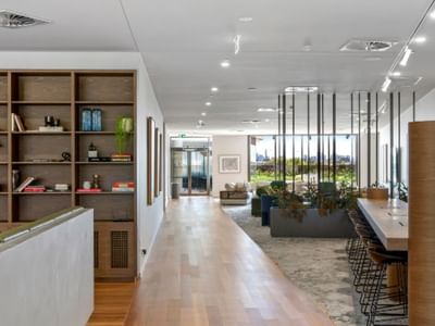 Modern communal hallway with wooden floor, bookshelves, lounge area, and large windows with city view.
