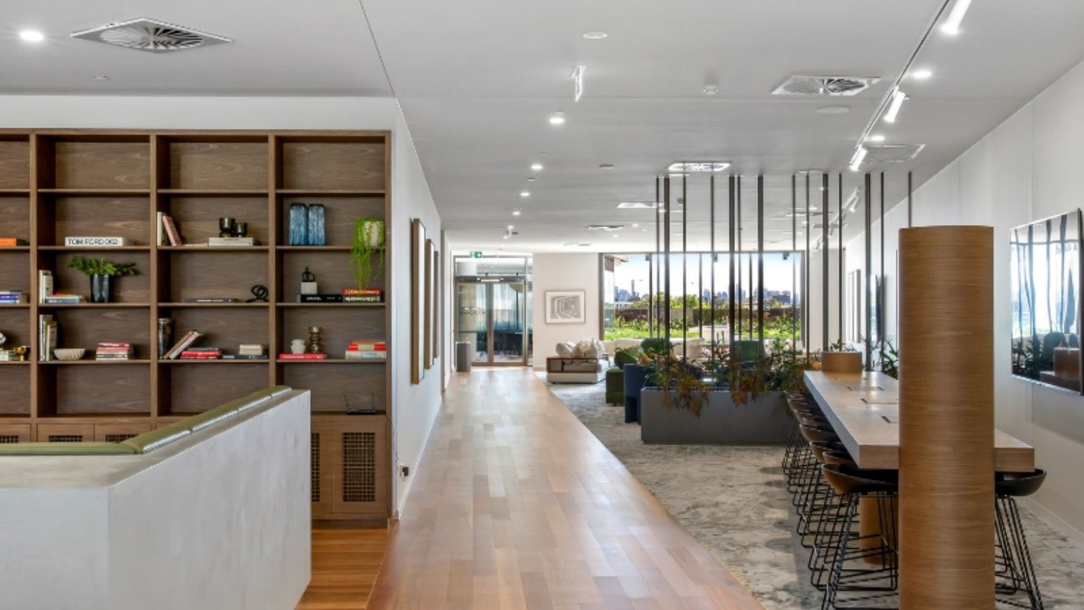 Modern communal hallway with wooden floor, bookshelves, lounge area, and large windows with city view.