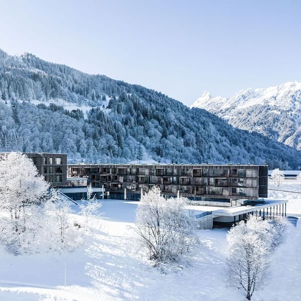 Exterior view of Falkensteiner Hotel Montafon surrounded by snow-covered trees with mountain backdrop