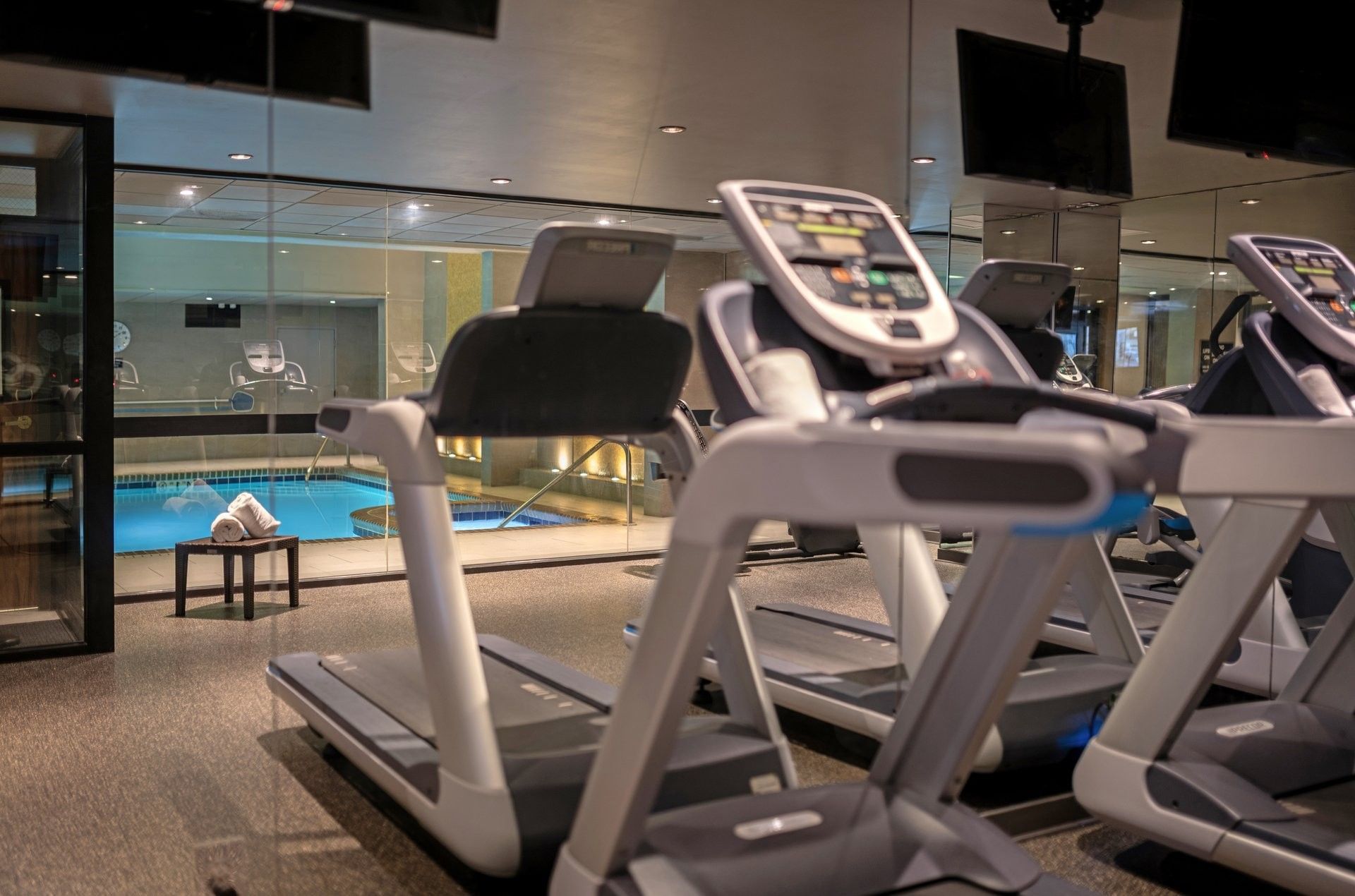 Treadmills in a fitness center by a glass wall overlooking an indoor pool at Warwick Seattle