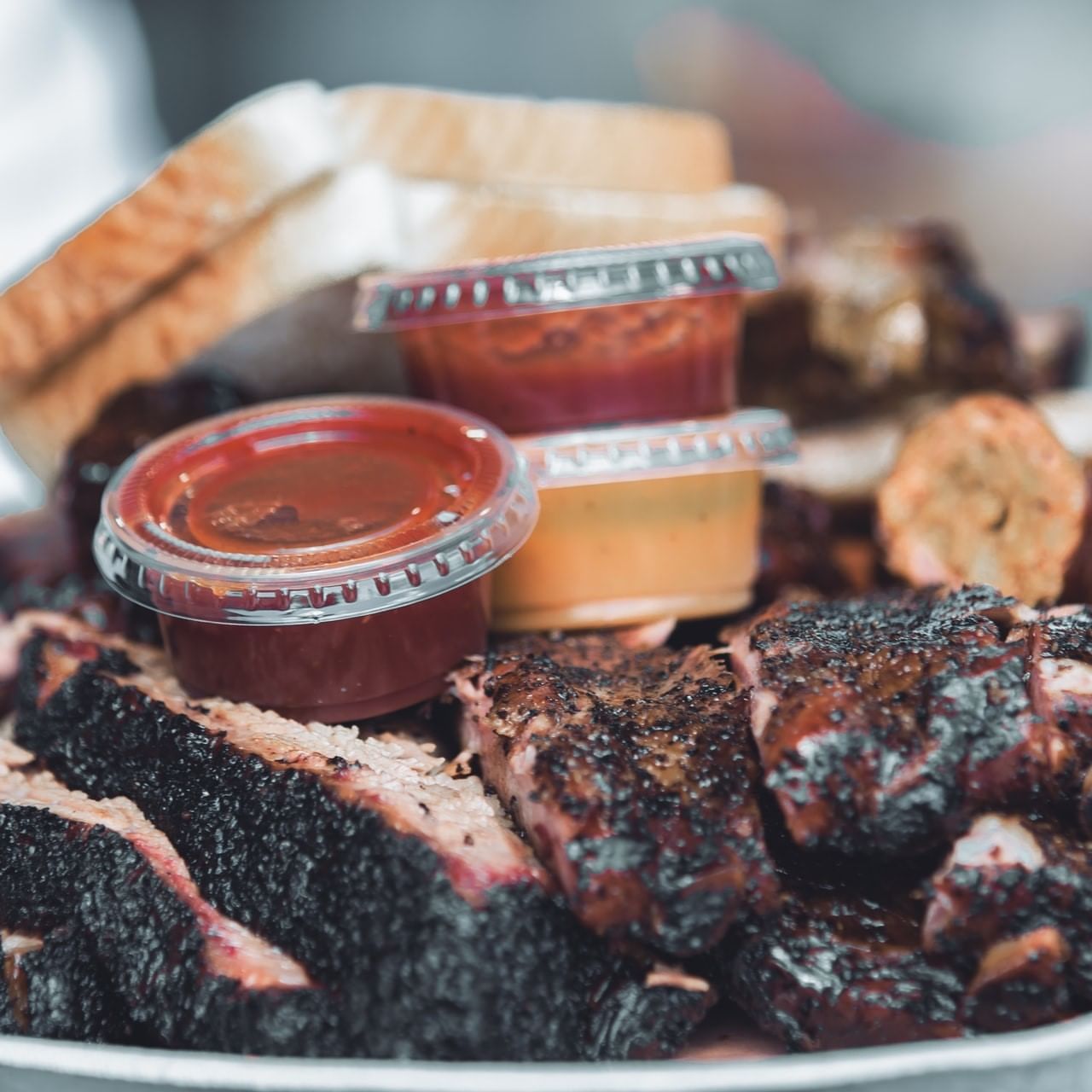 A closeup picture of barbeque meat with sauces and bread