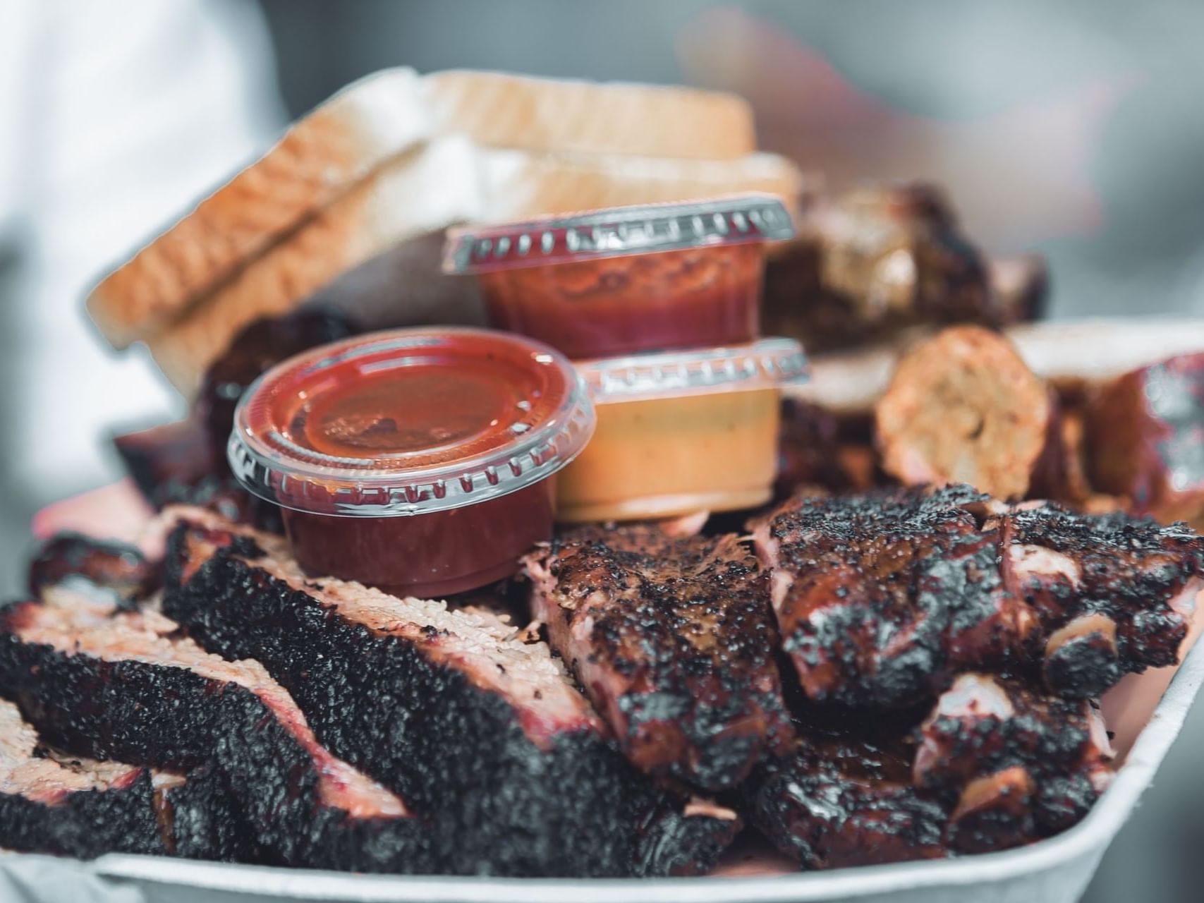 A closeup picture of barbeque meat with sauces and bread