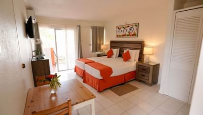 Dining table & chairs beside beds with orange runners near sliding patio door in Superior Room at Worthing Court Apartment