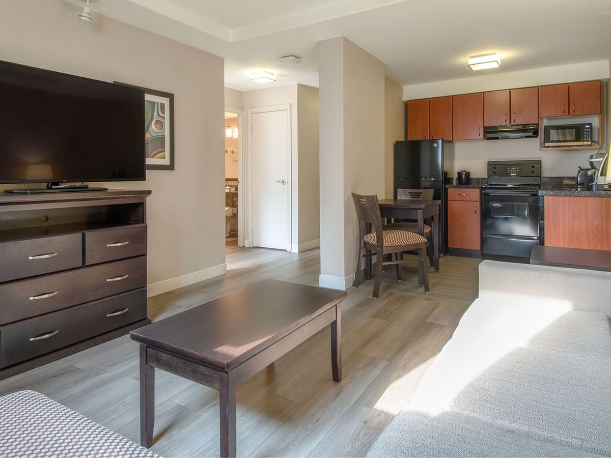 Hotel suite with TV, work desk, chair, table, and a kitchen area