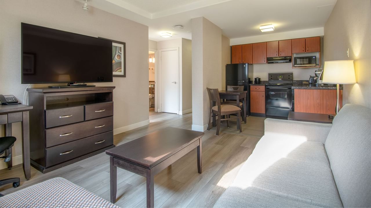 Hotel suite with TV, work desk, chair, table, and a kitchen area