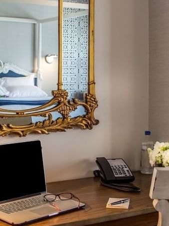 Laptop on a wooden desk by a gold mirror & white flowers under a grey wall in Loft Fireplace Suite at Warwick San Francisco