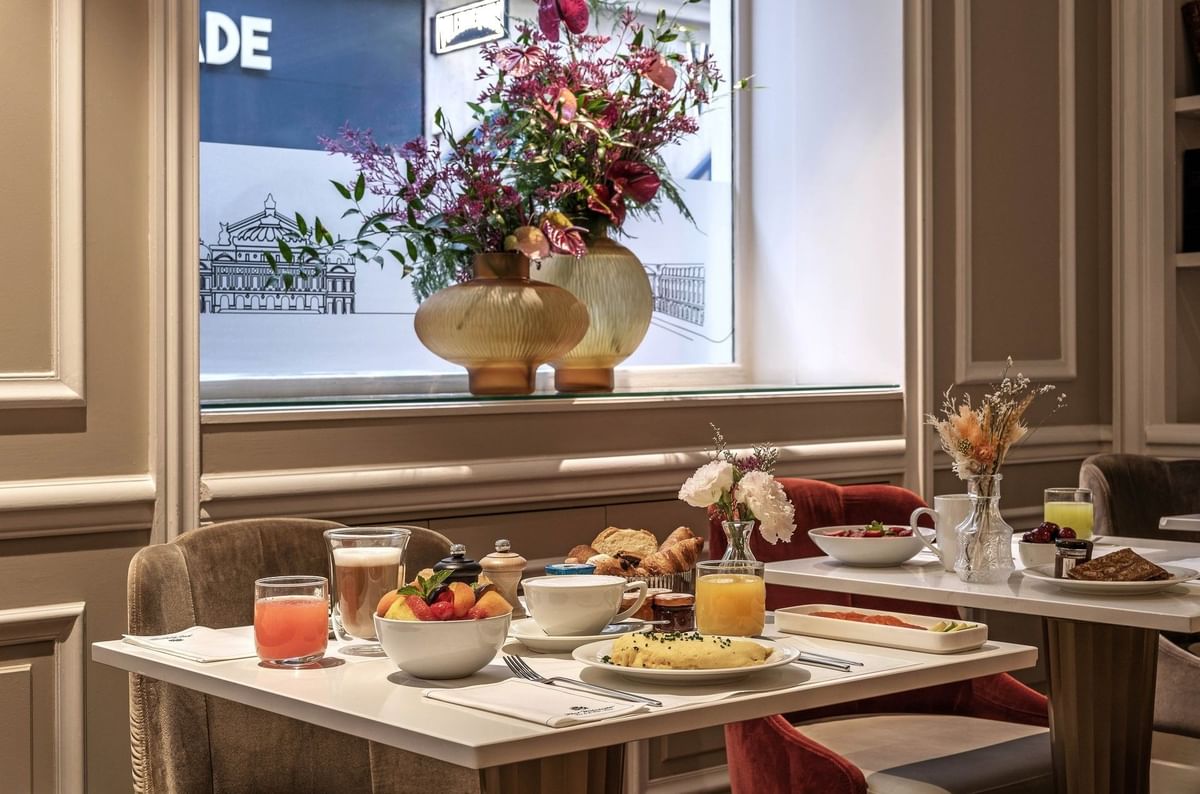 Breakfast service at Hotel Westminster Paris, featuring a plate of omelet and fruit by a window with floral vases
