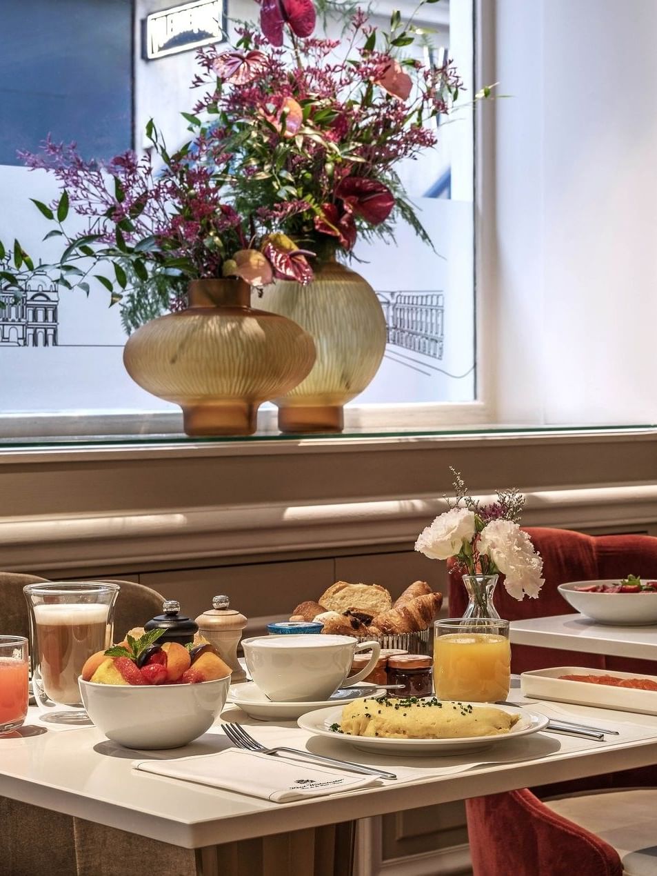 Breakfast service at Hotel Westminster Paris, featuring a plate of omelet and fruit by a window with floral vases