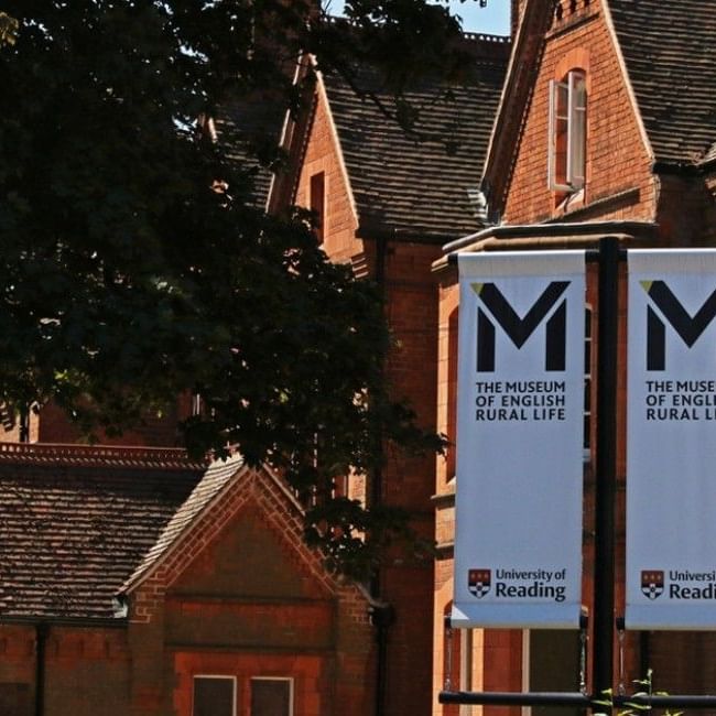 Red brick Victorian building with white banners displaying The Museum of English Rural Life logo in warm sunlight.