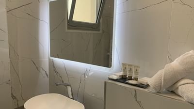 A modern bathroom with a sink, lit mirror, and folded towels on a counter.