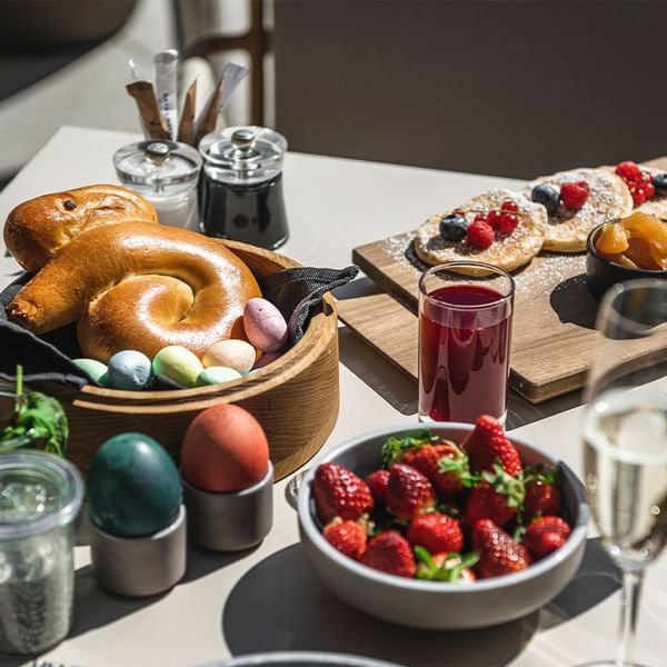 Table with brunch items including pastries, eggs, strawberries, and beverages at  Falkensteiner Hotels & Residences