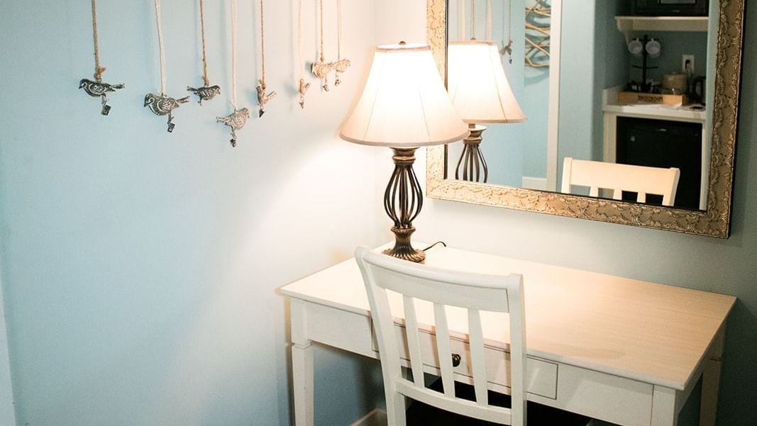 A hotel room with a white desk, chair, lamp, and mirror.
