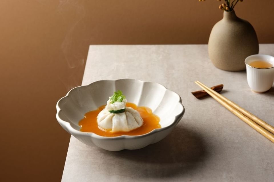 Close-up of a delicate pouch dumpling in a rich orange sauce served in a scalloped bowl at Carlton Hotel Singapore