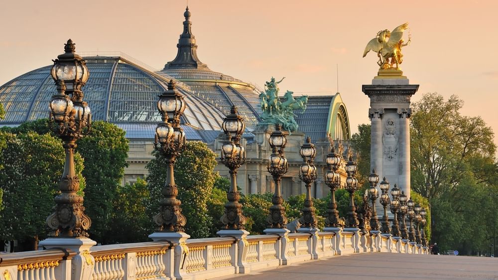 Row of ornate street lamps and bridge in Paris with a golden statue in background near Warwick Hotels & Resort