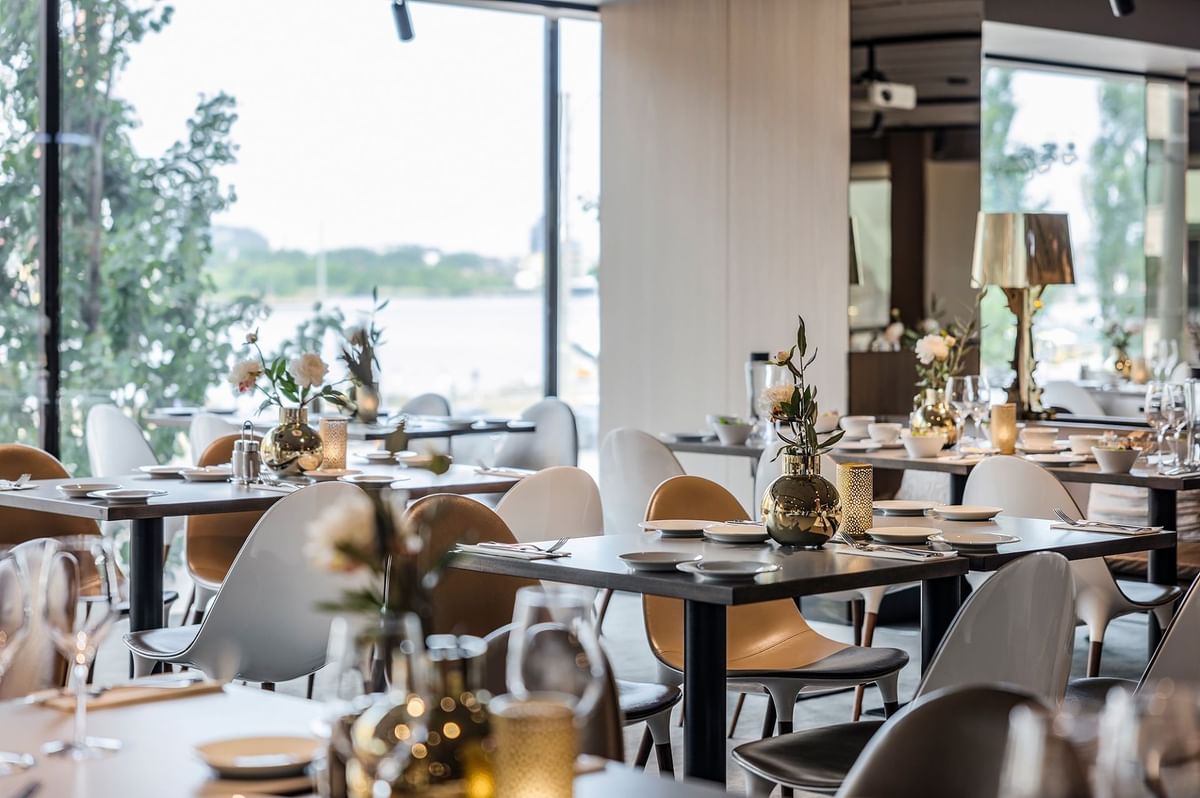 Restaurang med bord, stolar, blommor, ljus och vattenglas i en elegant och modern miljö.