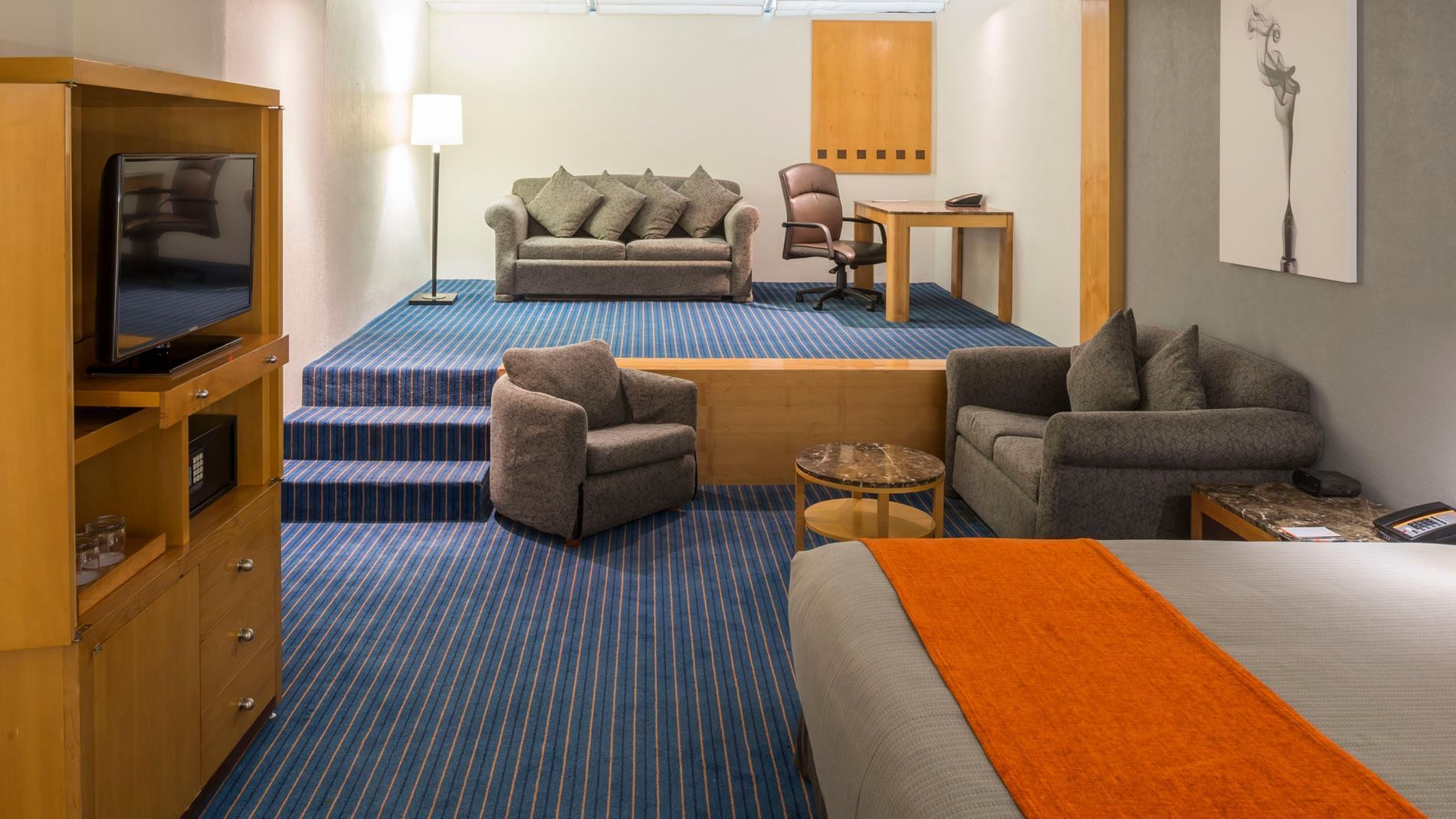 Lounge area in King Deluxe Superior featuring a sofa, desk, and view of the lower bedroom section at Real Inn Nuevo Laredo