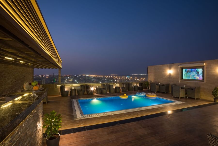 Rooftop pool, featuring wicker chairs & small tables under the clear night sky in Sky View Café at Naviti By Warwick Dammam