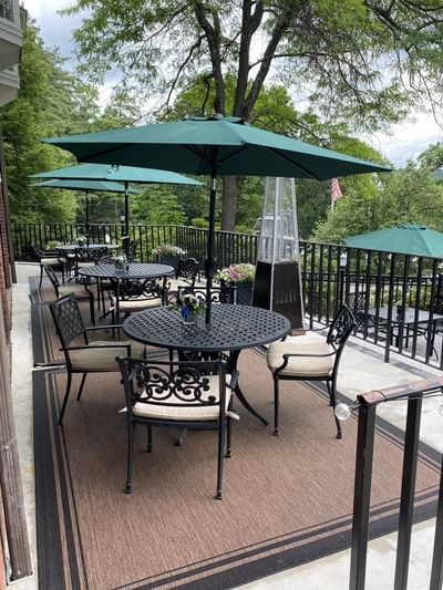 Spacious outdoor terrace with round tables, chairs, and green umbrellas set on brown rugs at The Simsbury Inn