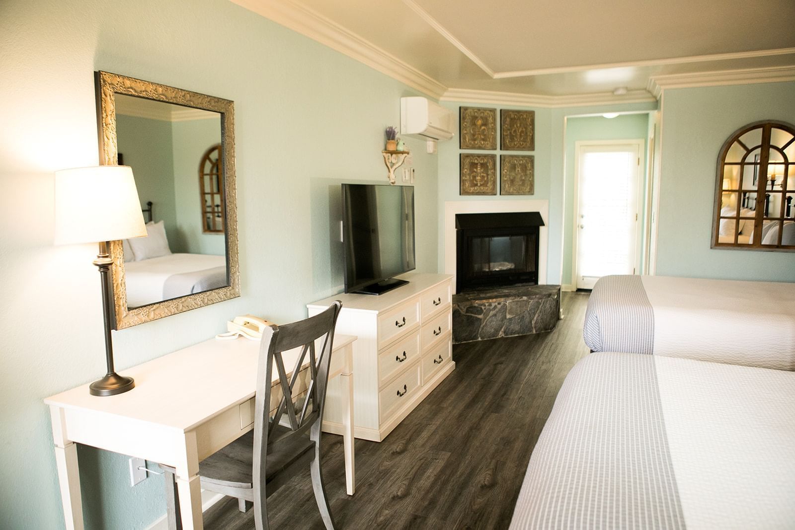 A hotel room with two queen beds, a desk, dresser, and fireplace.