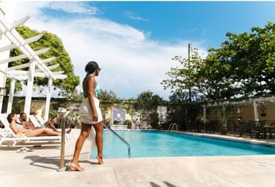 Woman walking by pool with guests on loungers at Courtleigh Hotel & Suites, an elite hotels in Kingston, Jamaica