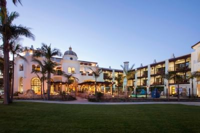 Stylish exterior of Santa Barbara Inn Hotel with palm trees, and outdoor seating, glowing in the evening light