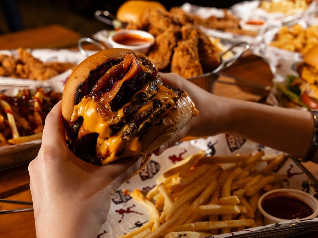 Cheeseburger with bacon & cheese being held over fries in KG Sport Bar at Mercure Brisbane King George Square