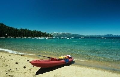 Red kayak rests on the sandy Lake Tahoe, with turquoise water and snow-capped mountains near Americana Village Suites