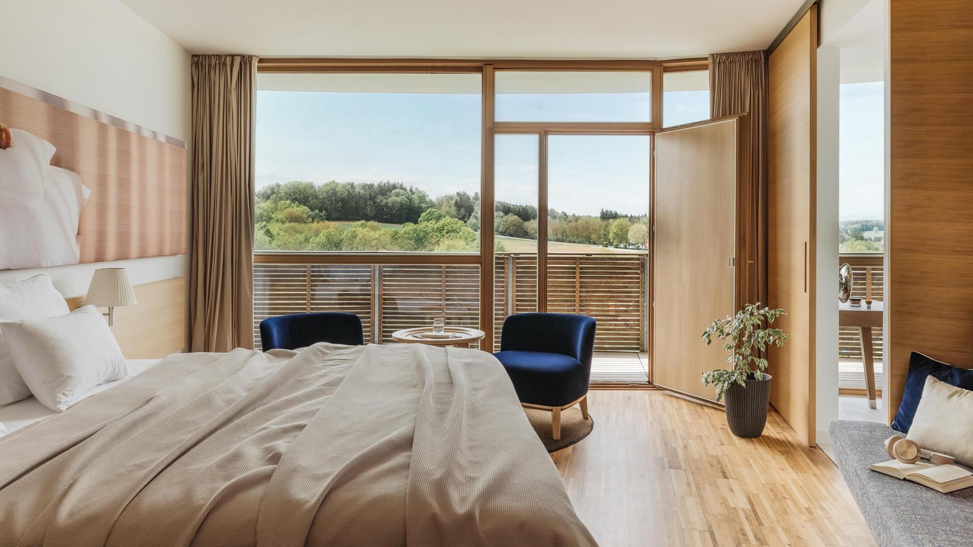 Hotelzimmer mit Bett, Sesseln, Balkon und Blick auf die Landschaft.