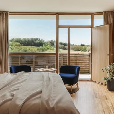 Hotelzimmer mit Bett, Sesseln, Balkon und Blick auf die Landschaft.