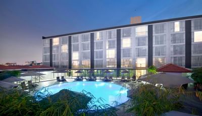 Hotel pool surrounded by pool beds with exterior of Eastin Grand Hotel Saigon