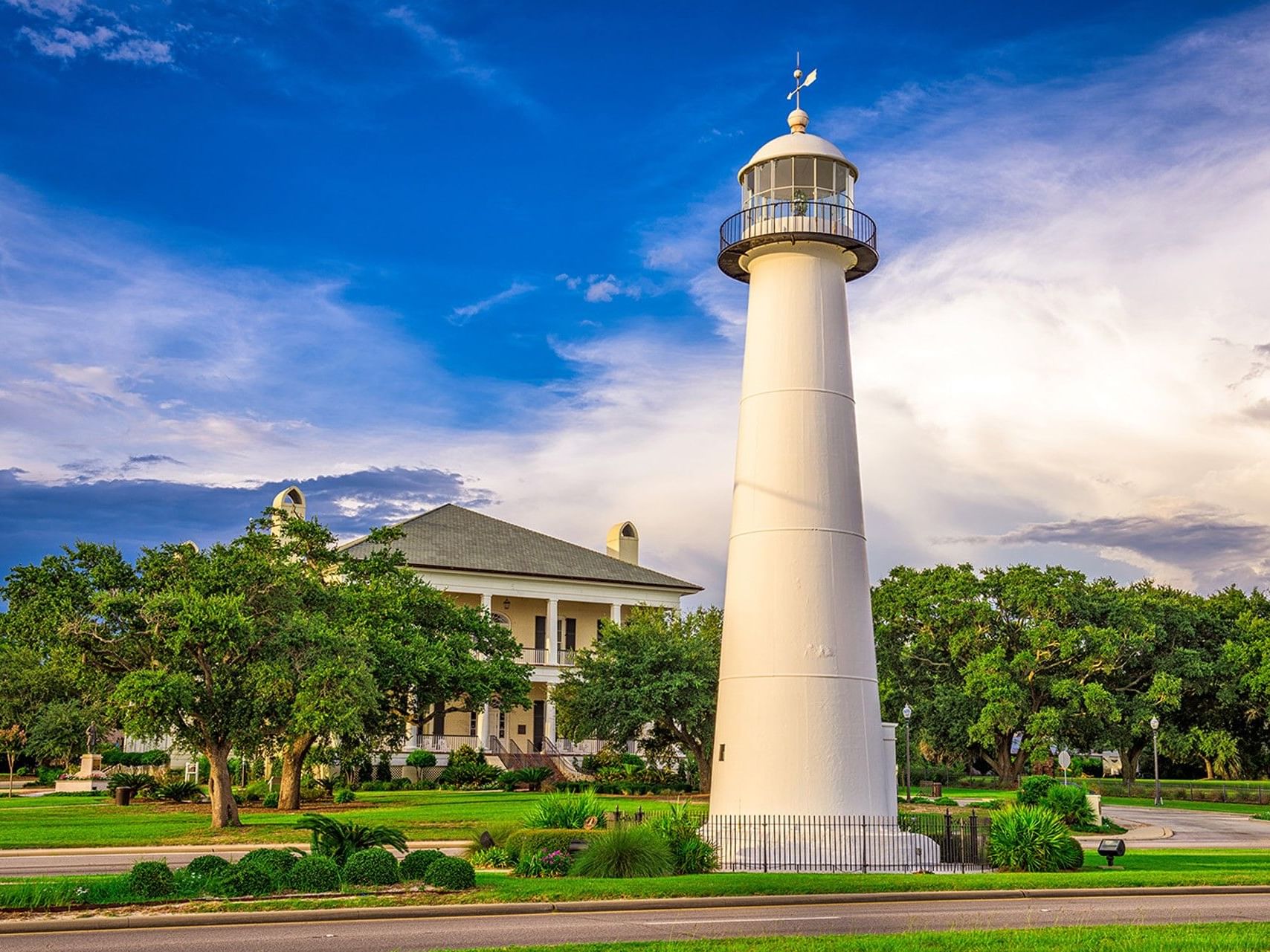 The iconic Biloxi Lighthouse stands in front of a large house and green trees near The White House Hotel