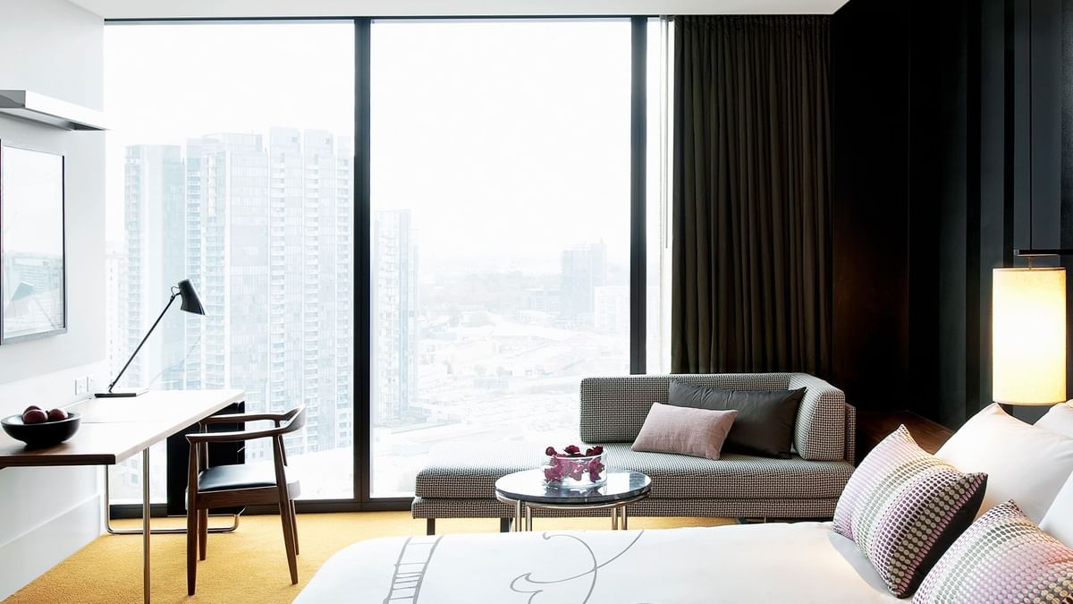 High Floor Luxe King with a large window overlooking city buildings, a bed, sofa, and desk area at Crown Hotel Melbourne