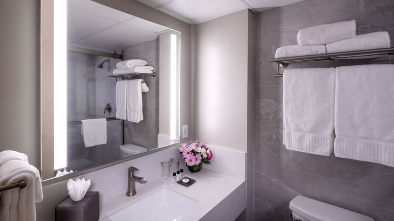 Modern bathroom with white sink, mirror, toilet, and towels, featuring flowers and tissue box at Warwick Hotels and Resorts
