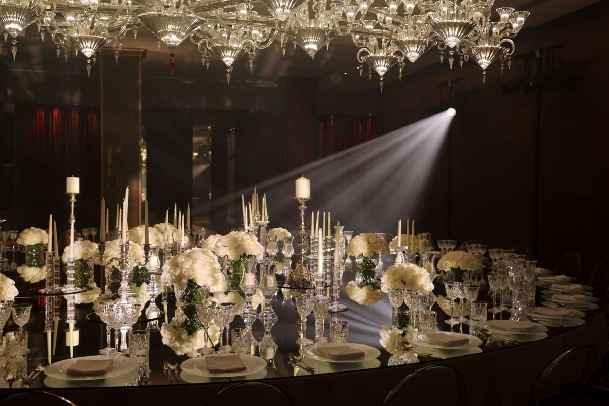 Elegantly set dining table with white flowers, candles, and crystal glasses under a chandelier at The May Fair Hotel.