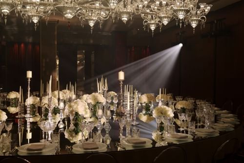 Elegantly set dining table with white flowers, candles, and crystal glasses under a chandelier at The May Fair Hotel.