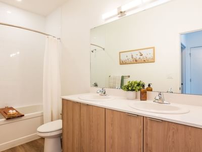 A modern and large three-piece bathroom includes a long cabinet with two sinks and plenty of storage space, a toilet and a bathtub shower.