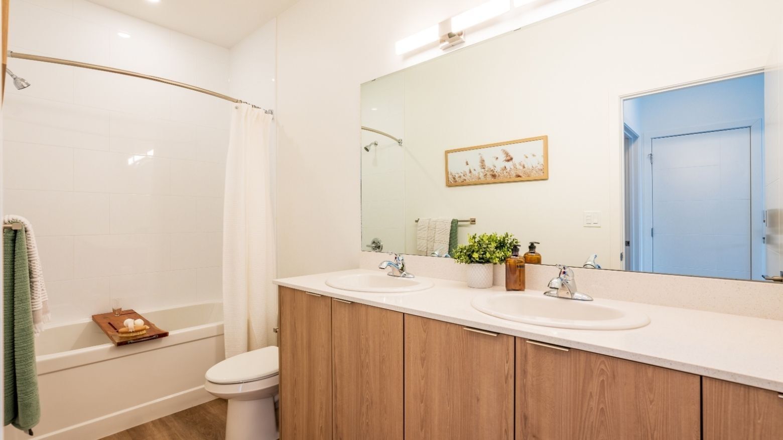 A modern and large three-piece bathroom includes a long cabinet with two sinks and plenty of storage space, a toilet and a bathtub shower.